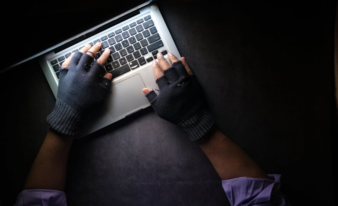 Close-up of hands typing on a laptop keyboard in low light, wearing fingerless gloves, symbolizing the proactive measures in cybersecurity through real-time threat intelligence.